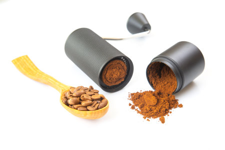 A modern manual coffee grinder, opened to show ground coffee, with some powder spilled on a white background, ideal for kitchen and coffee-related stock photography.の写真素材