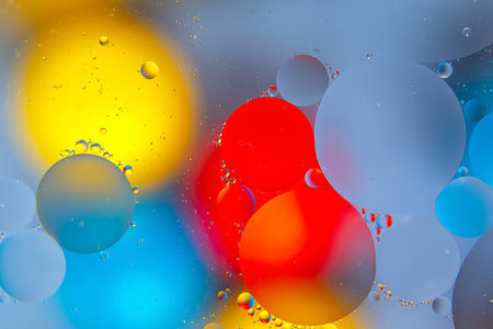 Colorful water droplets in red, yellow, blue, and green on a shiny surface, offering an abstract, creative background with a fresh look.の写真素材