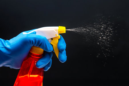 A gloved hand activates a red spray bottle with a yellow nozzle, releasing a fine mist on a black backdrop, perfect for cleaning product ads or sanitation themes.の写真素材