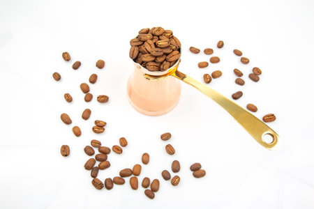 Vintage copper Turkish coffee maker with a golden handle beside a pile of coffee beans on a white background, great for traditional drink and culinary concepts.の写真素材
