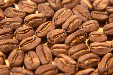 High-quality macro image of roasted coffee beans on a golden surface, emphasizing their rich color and cracked texture.の写真素材