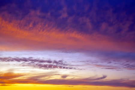 Dark and light clouds blend together in a stunning sunset sky. The sun's golden glow subtly illuminates the edges of the clouds, creating a dreamy and moody effect.の写真素材