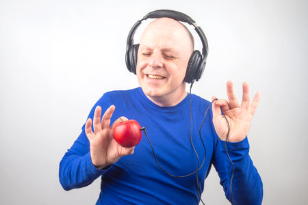 bald man with headphones listens to music through a red apple player. Metaphor and concept of vitamin benefits in music and soundの写真素材