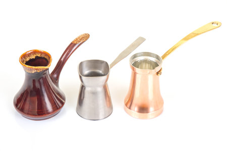 A set of three Turkish coffee pots in stainless steel, glazed ceramic, and copper with brass handles, isolated on a white background, ideal for coffee culture and kitchen decor photographyの写真素材