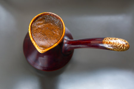 Close-up of a shiny cezve filled with frothy Turkish coffee on a sleek gray surface. Ideal for coffee culture, beverage ads, or minimalist kitchen decor.の写真素材