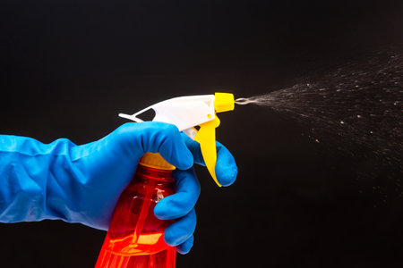 blue-gloved hand using a red spray bottle with a yellow trigger, mist in motion against a dark background, great for household cleaning or safety visuals.の写真素材