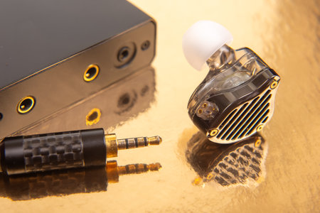 An earbud, a 3.5mm audio jack, and a black audio device on a gold surface, great for showcasing tech accessories and sound equipment.の写真素材