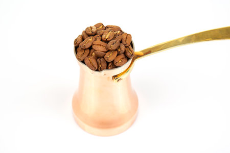 Authentic copper coffee pot with a brass next handle to a spread of coffee beans on a white surface, excellent for cultural heritage and beverage photographyの写真素材