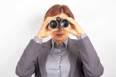Business woman in suit looking through binocularsの写真素材