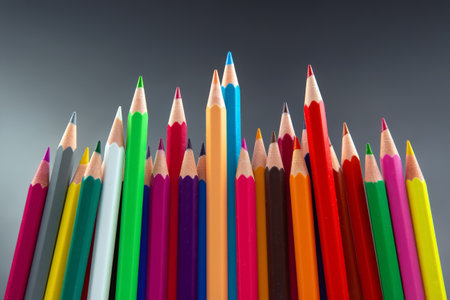 Colorful pencils arranged in a wave-like pattern, showing a spectrum of hues from yellow to green. Ideal for back-to-school, drawing, or artistic projects on a soft gray backdrop.の写真素材