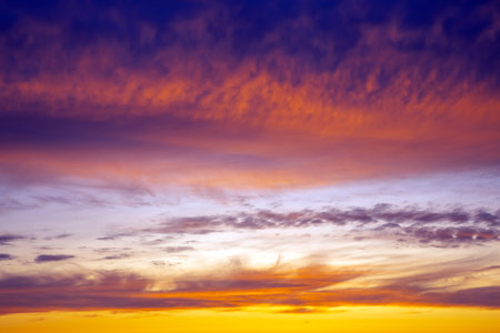 Vibrant sunset over the horizon with a colorful sky of orange, pink, and blue hues. Scattered clouds reflect the sunlight, creating a serene and picturesque scene, perfect for natureの写真素材