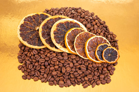 Golden reflective surface hosts coffee beans and dried orange slices, a perfect shot for aromatic food compositions. coffee aroma and taste citrus descriptorsの写真素材
