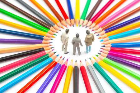 Three small figurines stand in the center of a vibrant circle of colorful pencils, symbolizing creativity and unity on a white background.の写真素材