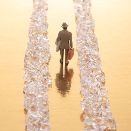 A small businessman walks between gleaming crystal piles on a reflective golden floor, representing a journey toward riches and achievementの写真素材