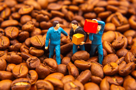 A creative close-up of three miniature figures in blue uniforms exchanging a yellow box and a red package amidst a sea of coffee beans, symbolizing trade or commerce.の写真素材