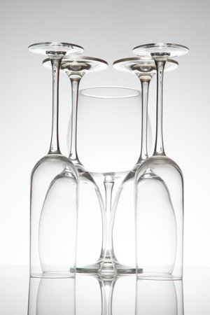 Crystal wine glasses in various shapes stand tall, their reflections doubling on a sleek surface, captured against a soft gray backdrop for fine dining concepts.の写真素材