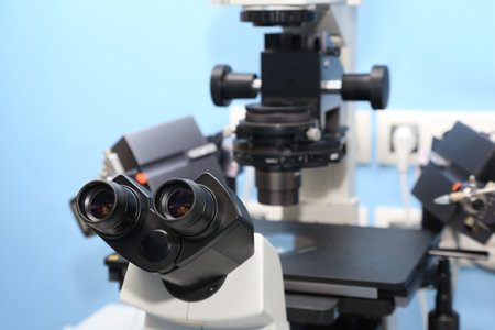 A scientist in a blue cap examines a sample under a high-tech microscope in a lab, with a petri dish...