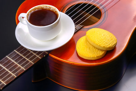 A steaming cup of coffee sits beside two yellow cookies on a wooden guitar. The warm colors create a cozy atmosphere, perfect for a relaxing afternoon filled with music and treats.の写真素材
