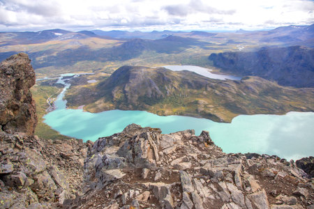 Stunning panoramic view from a mountain summit showcases the vibrant turquoise lakes surrounded by lush green landscapes in Norway. The clear view highlights the natural beauty of the region.の写真素材