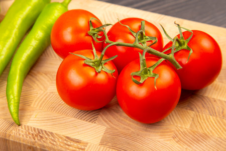 Bright red tomatoes sit on a wooden cutting board alongside vibrant green peppers, showing fresh produce ready for meal preparation. Perfect for salads, sauces, or culinary creations.の写真素材