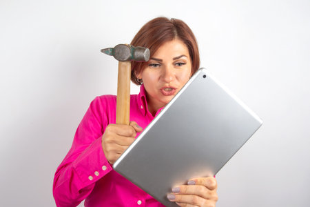 A woman wearing a bright pink shirt displays frustration while holding a hammer and staring at a...