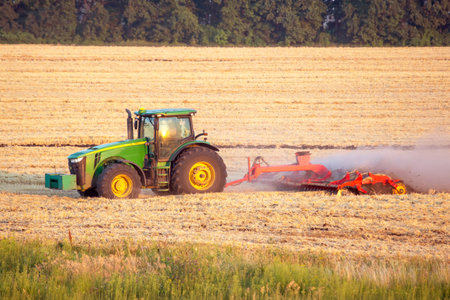A tractor is plowing a large agricultural field as the sun rises, casting golden light over the...