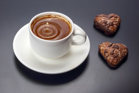 A cup of rich hot chocolate sits on a white saucer, accompanied by two heart-shaped cookies. The...