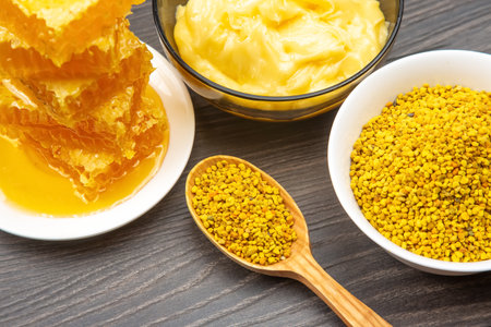 A wooden table showcases an assortment of natural bee products including golden honeycomb, yellow...