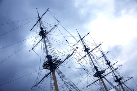 Masts of a historic ship stand prominently against a moody, overcast sky. The scene captures the...