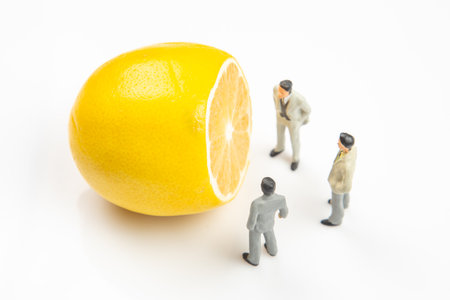 Three miniature figures in suits gather around a gigantic lemon, seemingly engaged in conversation about its size.の写真素材