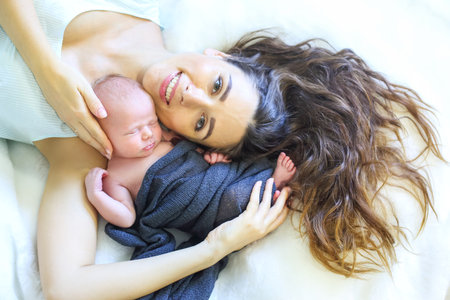 A mother cradles her newborn baby in a cozy setting, highlighting their bond. The soft blanket adds...