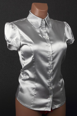 A stylish silver satin blouse featuring puff sleeves is displayed on a mannequin against a dark background. The blouse has a fitted design and button closure, perfect for chic occasions.の写真素材