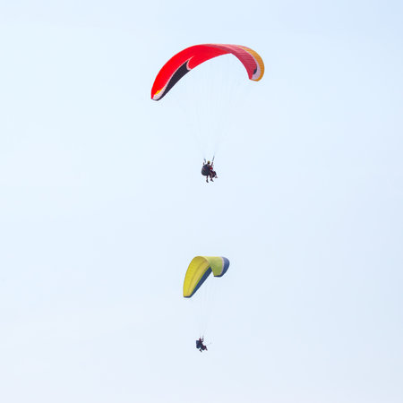 Two paragliders glide gracefully through a clear sky, showcasing their colorful canopies against a...