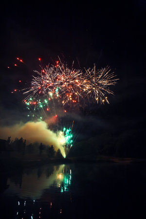Fireworks burst in vibrant colors above a peaceful lake, reflecting the dazzling lights on the water. This festive display takes place during a summer night, captivating onlookers with joy.の写真素材