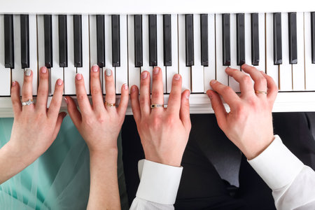 Two pairs of hands elegantly dance across piano keys, while the individuals enjoy a lively time together. The elegant setting radiates warmth and creativity as they share their musical skills.の写真素材