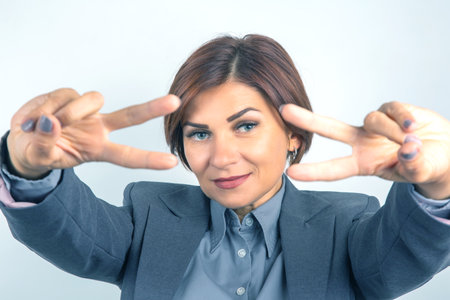 A woman with short brown hair and blue eyes smiles cheerfully while making peace signs with her fingers.の写真素材