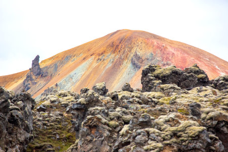 Vibrant hues dominate the volcanic terrain in Iceland, showcasing a breathtaking mountain backdrop and rugged lava formations. Nature's artistry is on full display against a cloudy sky.の写真素材