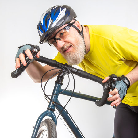 A mature cyclist dressed in a bright yellow shirt and wearing a helmet is adjusting the handlebars of his bike. He appears focused and ready for his next adventure in cycling.の写真素材