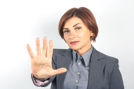 The woman stands confidently in a business suit, raising her hand in a stop gesture.の写真素材