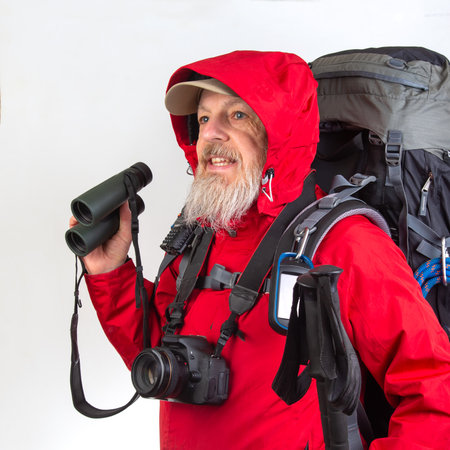 Outdoor enthusiast wearing a red jacket stands ready for exploration, holding binoculars and a camera. The rugged backpack indicates preparation for an adventure in nature.の写真素材