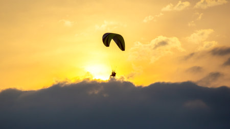 A paraglider glides gracefully through the soft clouds during sunset, with vibrant colors illuminating the sky. This serene moment captures the thrill of flying amidst nature's beauty.の写真素材