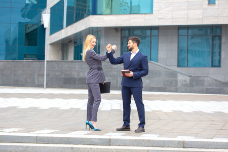 Two professionals in business attire engage in a celebratory gesture on a city street.の写真素材