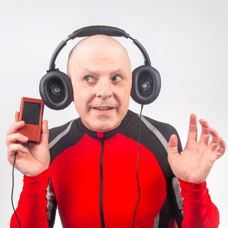 A man listens to music using large headphones while holding a portable music device. He wears a bright red athletic outfit and appears to be enjoying the moment of relaxation and enjoyment.の写真素材