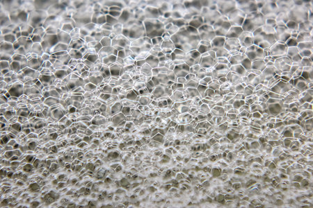 Bubbles create a captivating, textured surface with a hexagonal pattern, reflecting light beautifully. The close-up reveals the delicate structures and transparent qualities of the soap film.の写真素材
