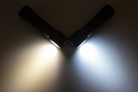 Two flashlights are positioned at an angle, casting beams of warm and cool light. Their illumination highlights the surrounding darkness, perfect for exploring unknown areas at night.の写真素材