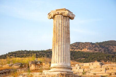 A well-preserved column stands tall against the backdrop of rolling hills at sunset in Turkey. The...