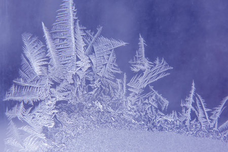 Delicate frost crystals are beautifully formed on a window, showing intricate patterns. The icy...