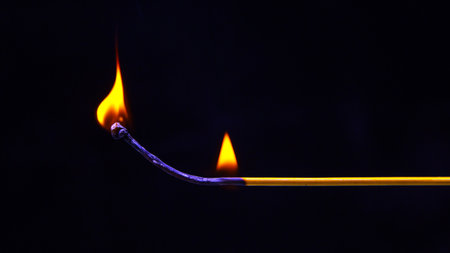 A colorful incense stick burns brightly, producing two vibrant flames against a dark background. The soft glow enhances the atmosphere, suggesting an evening of calm and tranquility.の写真素材