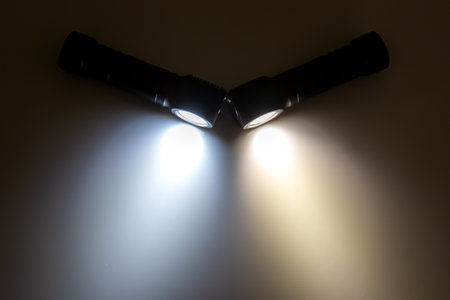 Two angled flashlights illuminate the darkness with bright white and softer yellow beams, showing the dynamic effects of light in a low-light setting.の写真素材