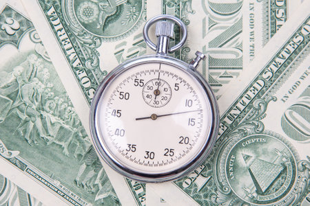 A stopwatch is placed on a background of one dollar bills, symbolizing the relationship between time and money.の写真素材